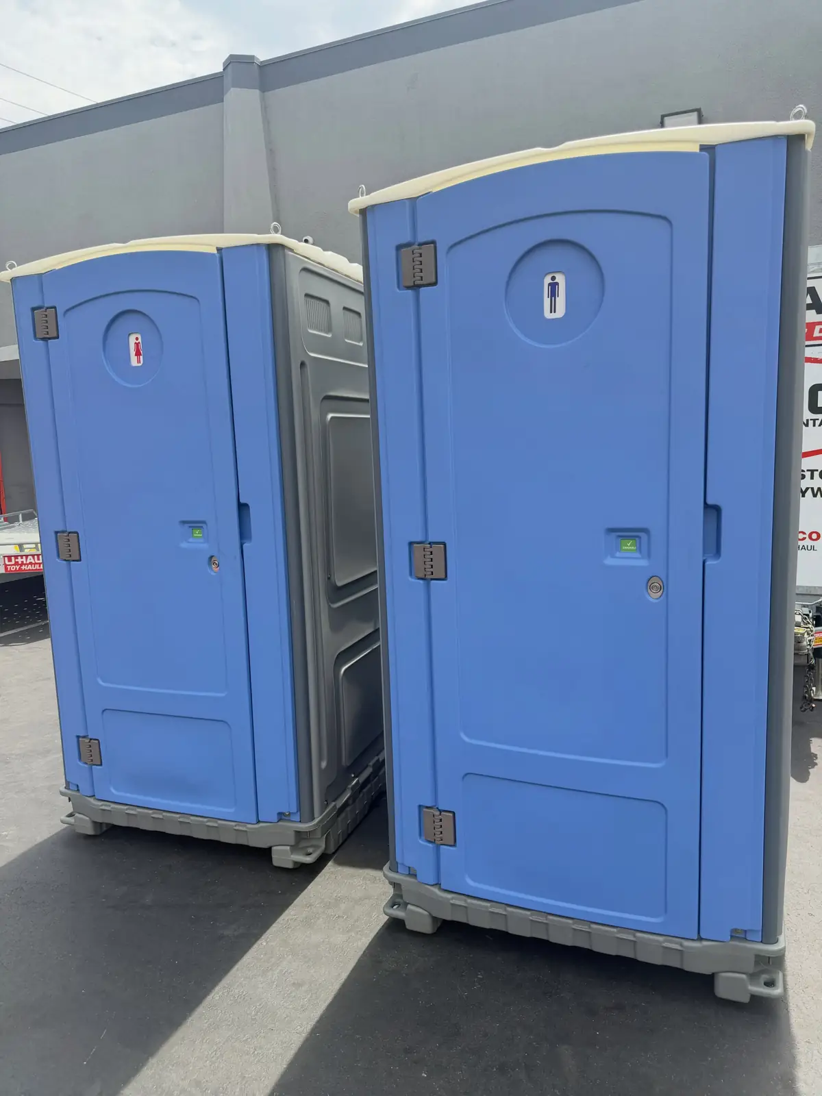 Two blue standard porta potties standing side by side in bright summer sun