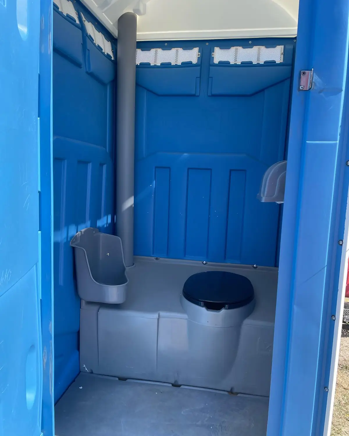 Inside a standard porta potty showing the toilet seat and a wall urinal